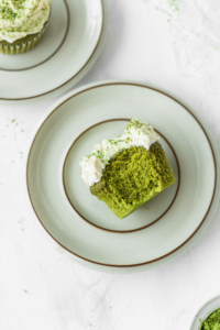 Half-eaten fluffy matcha cupcake with white chocolate frosting on a plate