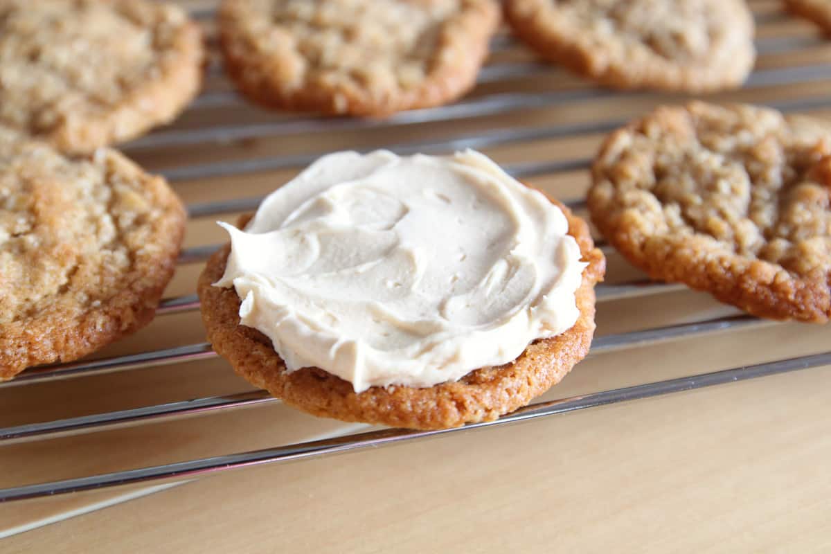 An oatmeal cookie on a wire rack with some buttercream frosting spread on top.