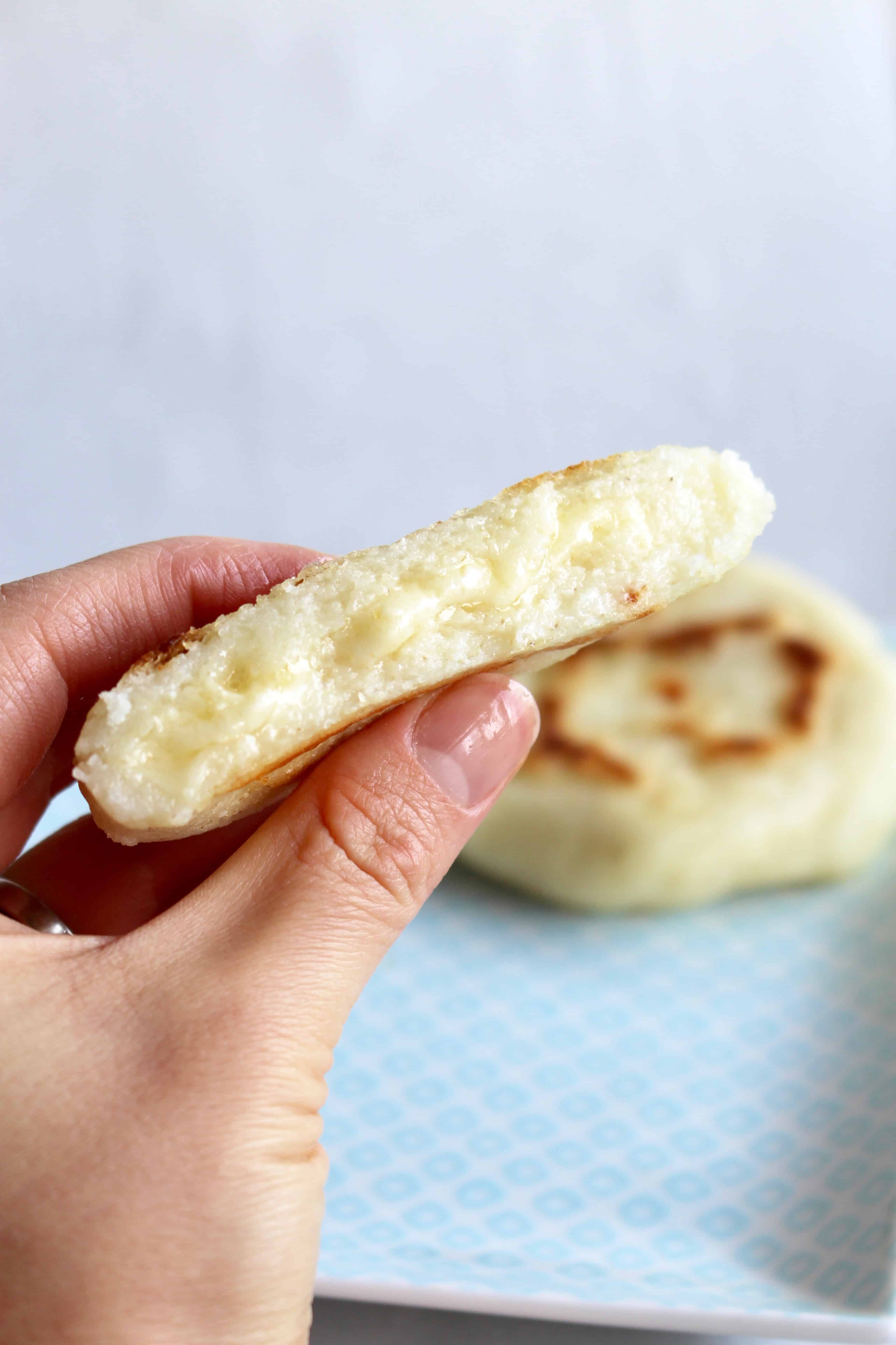 A hand holding an arepa with melty cheese stuffed inside.