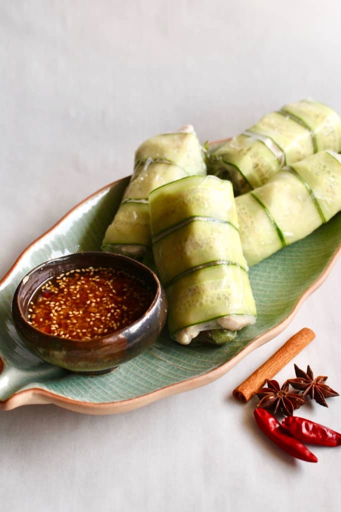 Spicy chicken summer rolls on a green dish with a small bowl of chili oil.