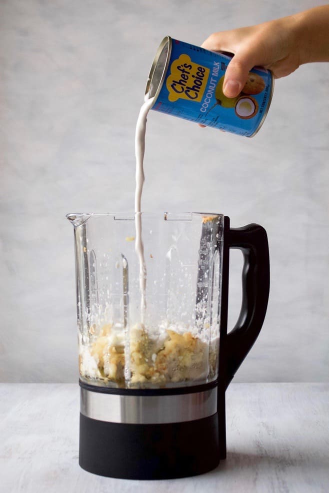A can of coconut milk being poured into a blender.