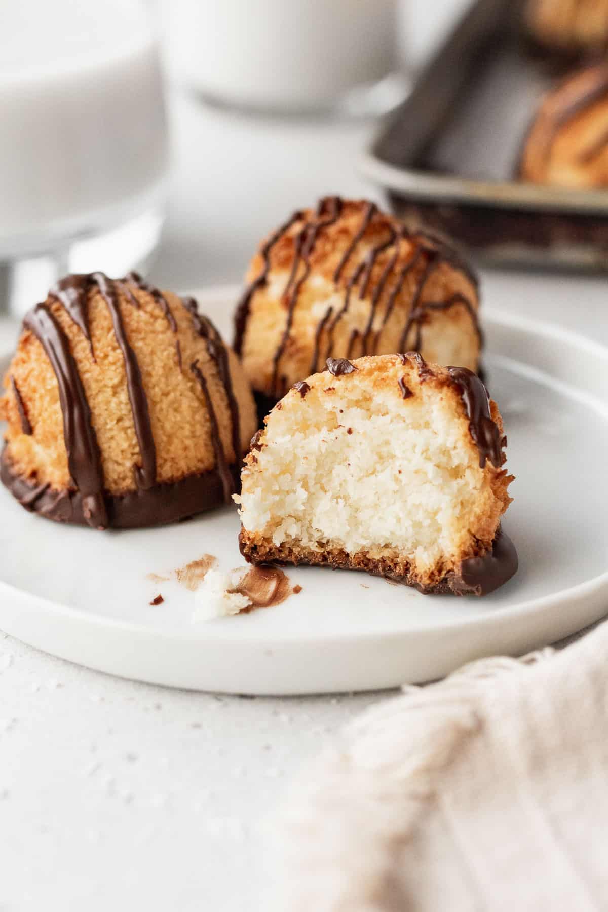 3 gluten free vegan macaroons on a white plate with one with a bite taken out of it.