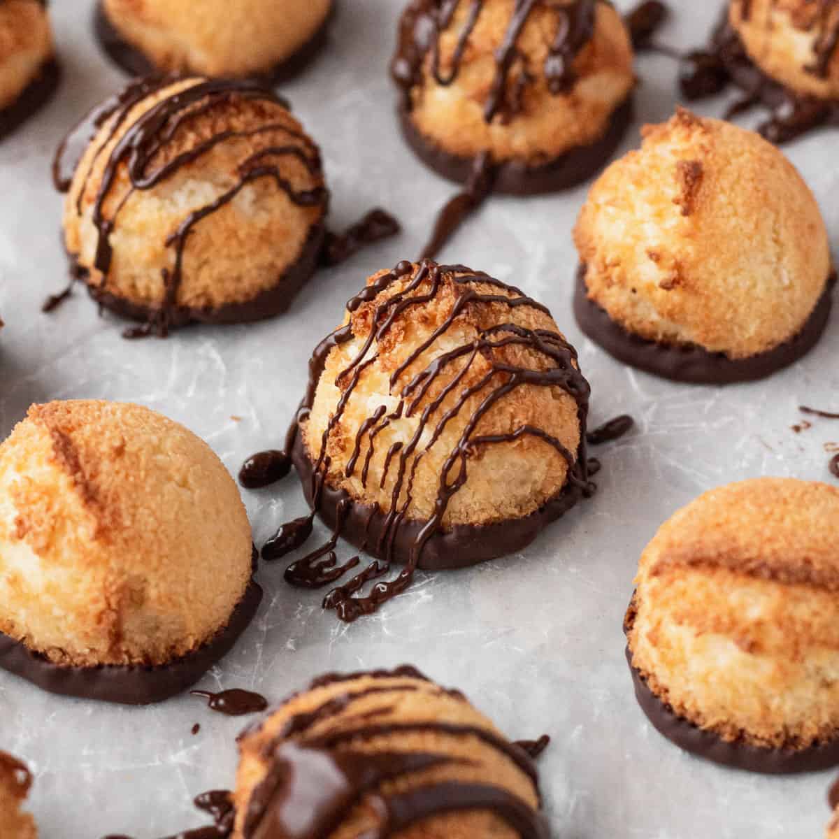 Plain and chocolate drizzled vegan coconut macaroons on a white surface.