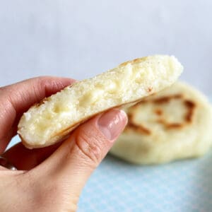 A hand holding an arepa with cheese.