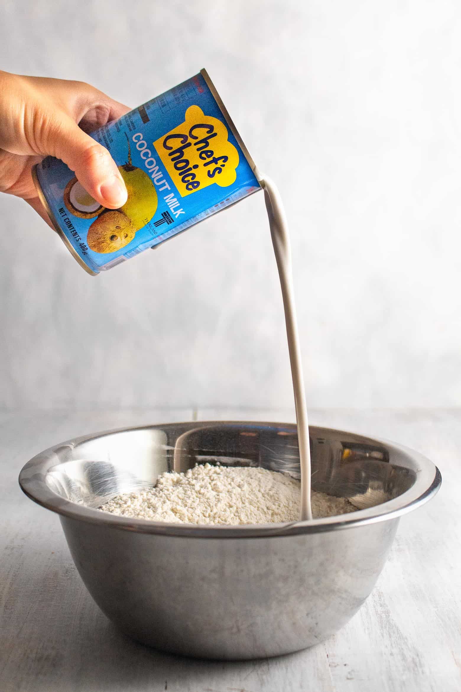 A can of coconut milk being poured into a bowl of flour.