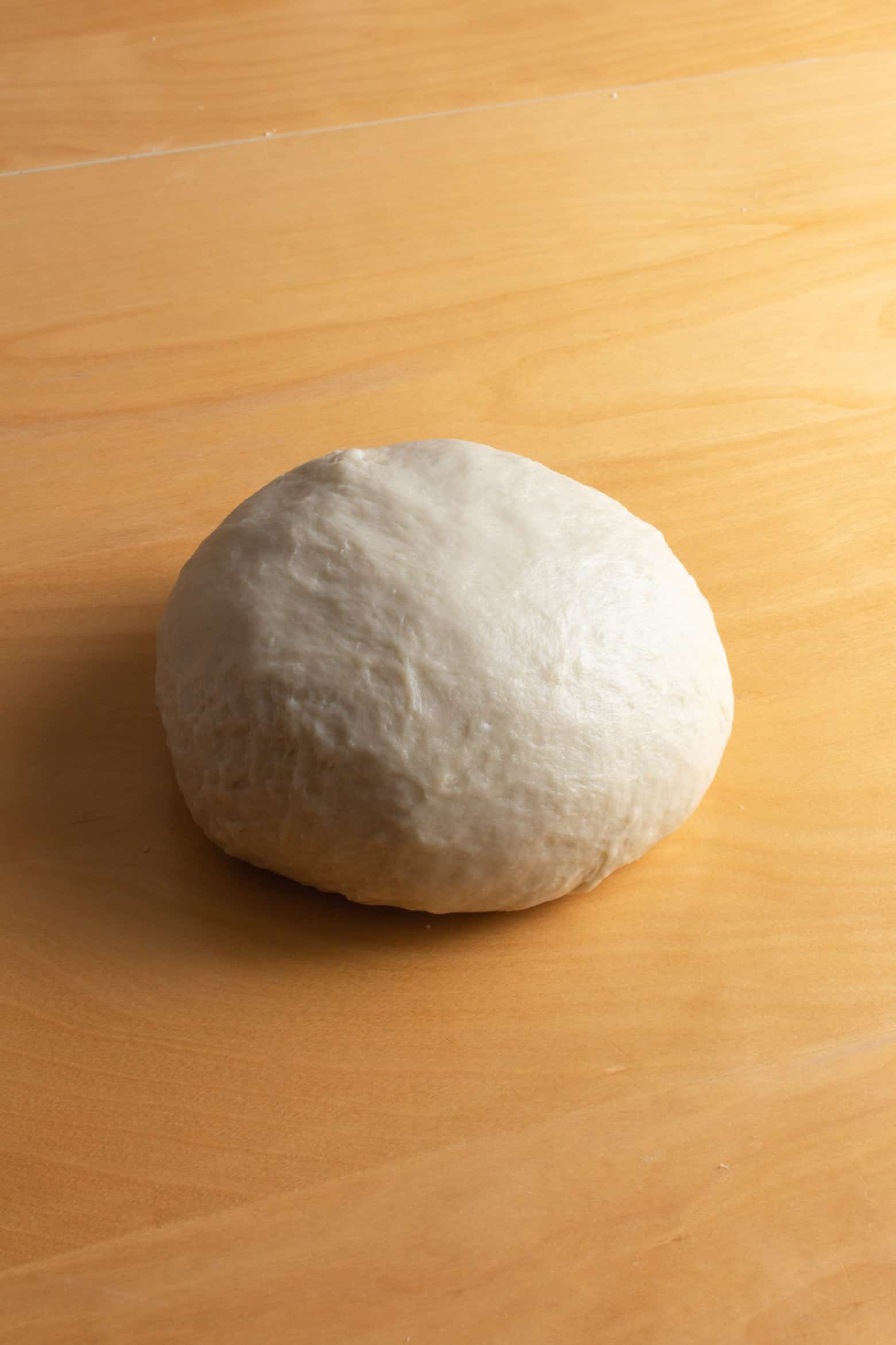 Kneaded ball of bread dough on a wooden surface.
