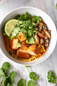 This vegan Thai red curry ramen is your new go-to quick and easy comfort food! Red curry paste and coconut milk make the perfect spicy and creamy soup for ramen noodles, deep fried tofu, and sautéed shiitake mushrooms. The scallions, cilantro, and lime juice tie it all together in this vegan fusion deliciousness! #veganrecipe #veganramen #thairedcurry #currypaste #coconutmilk