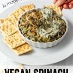 A cracker being dipped into a dish of vegan spinach artichoke dip with text overlay.