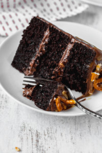 A fork cutting a bite out of a slice of moist chocolate cake with peanuts and pretzels