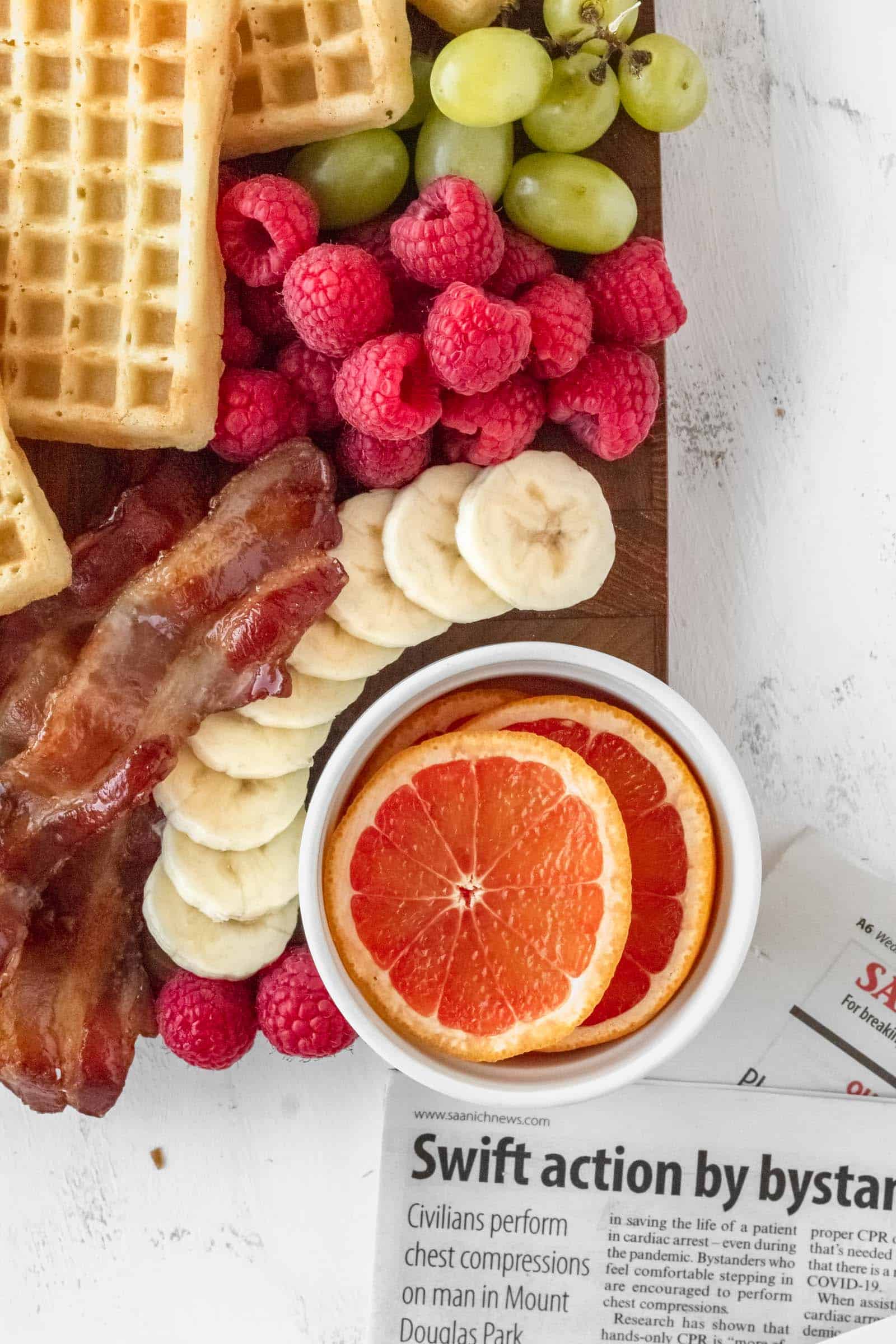 Green grapes, red raspberries, sliced bananas, oranges, and bacon on a breakfast charcuterie board