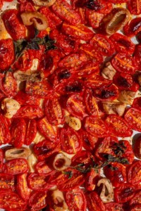 Close up of roasted cherry tomatoes, vegan calamari, garlic, and fresh oregano
