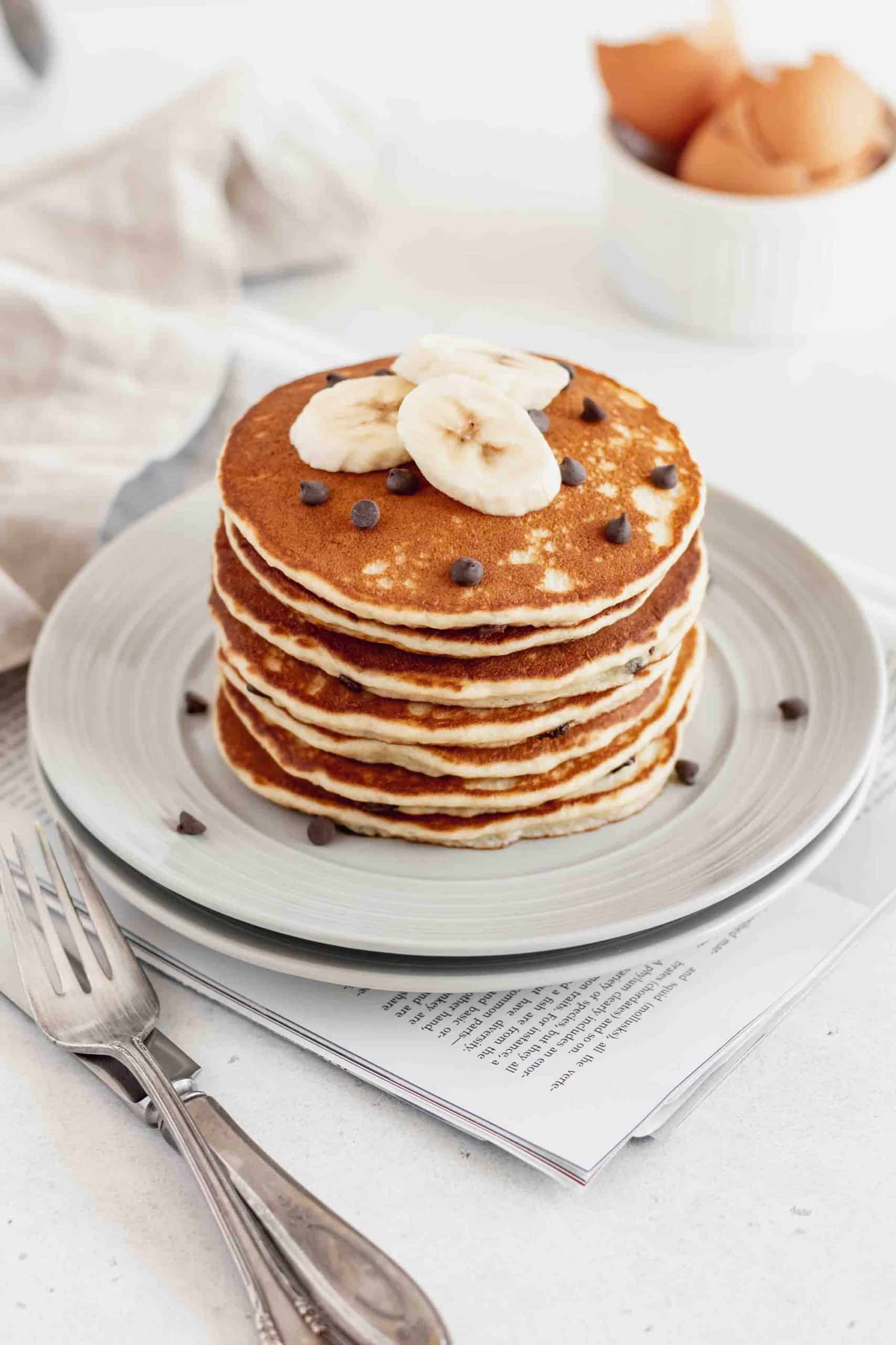 A stack of banana chocolate chip pancakes on a couple gray plates.