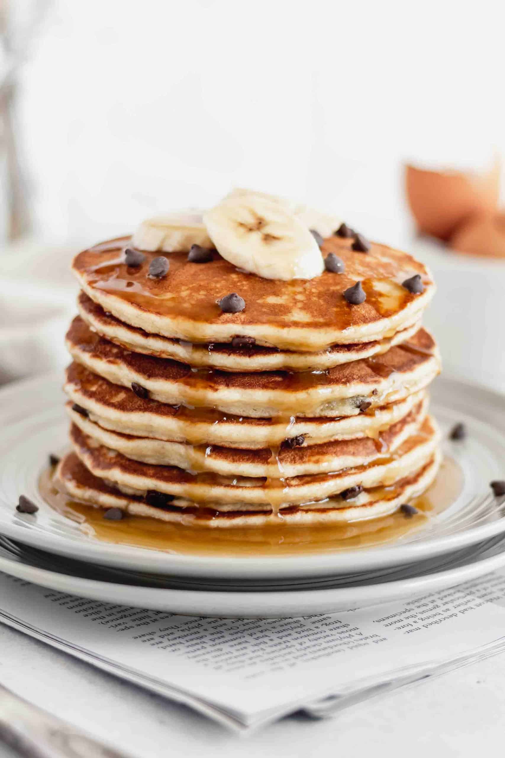 A stack of gluten free pancakes with slices bananas and chocolate chips on top, drizzled with maple syrup.