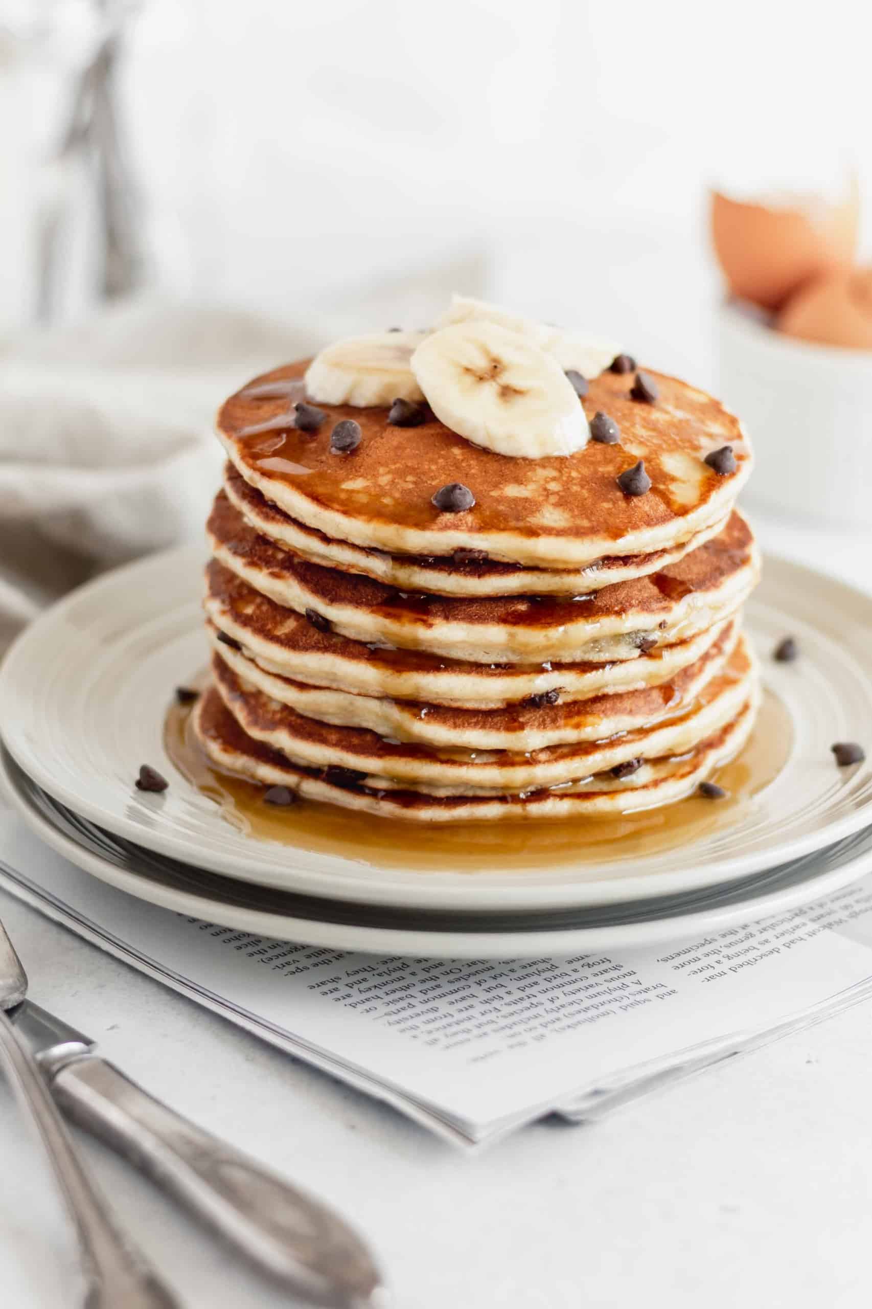 A stack of gluten free banana pancakes on a plate with slices of banana on top.