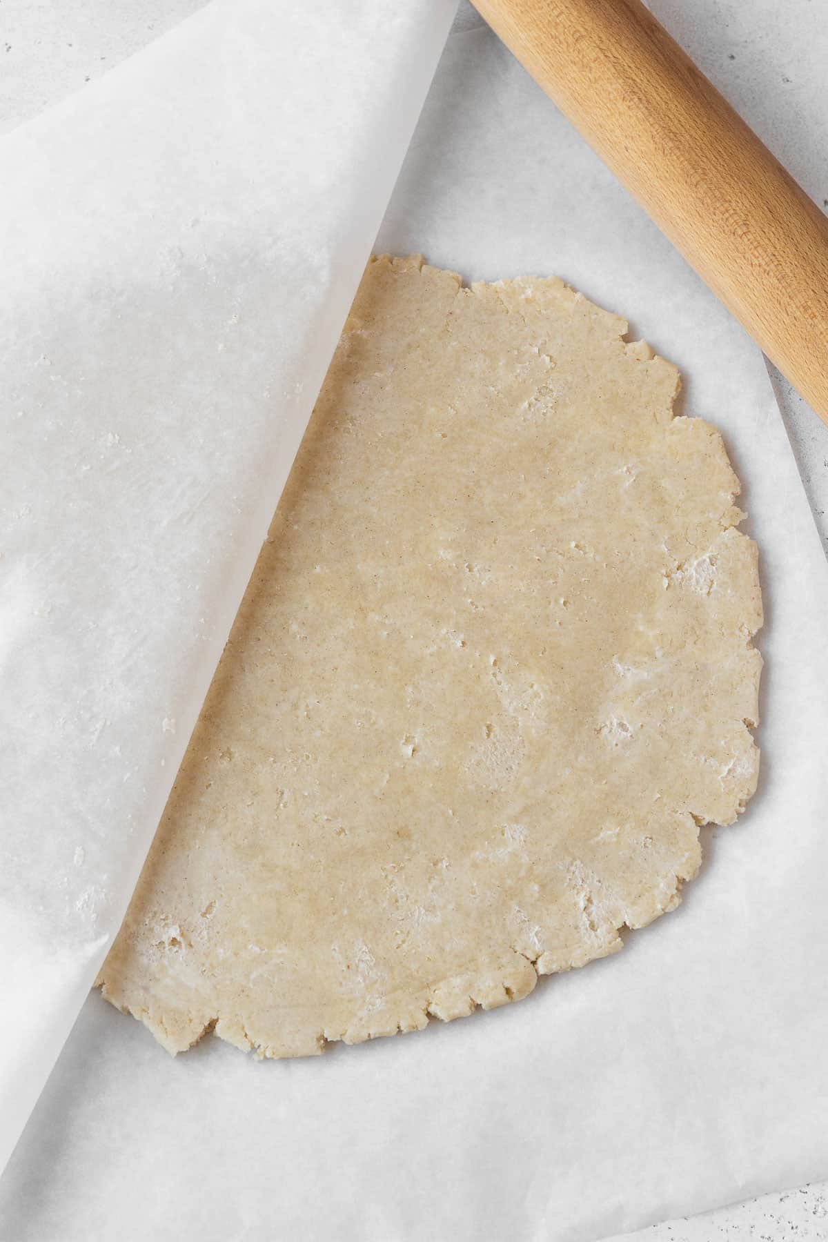 Dairy-free pie dough being rolled out between two sheets of parchment paper.