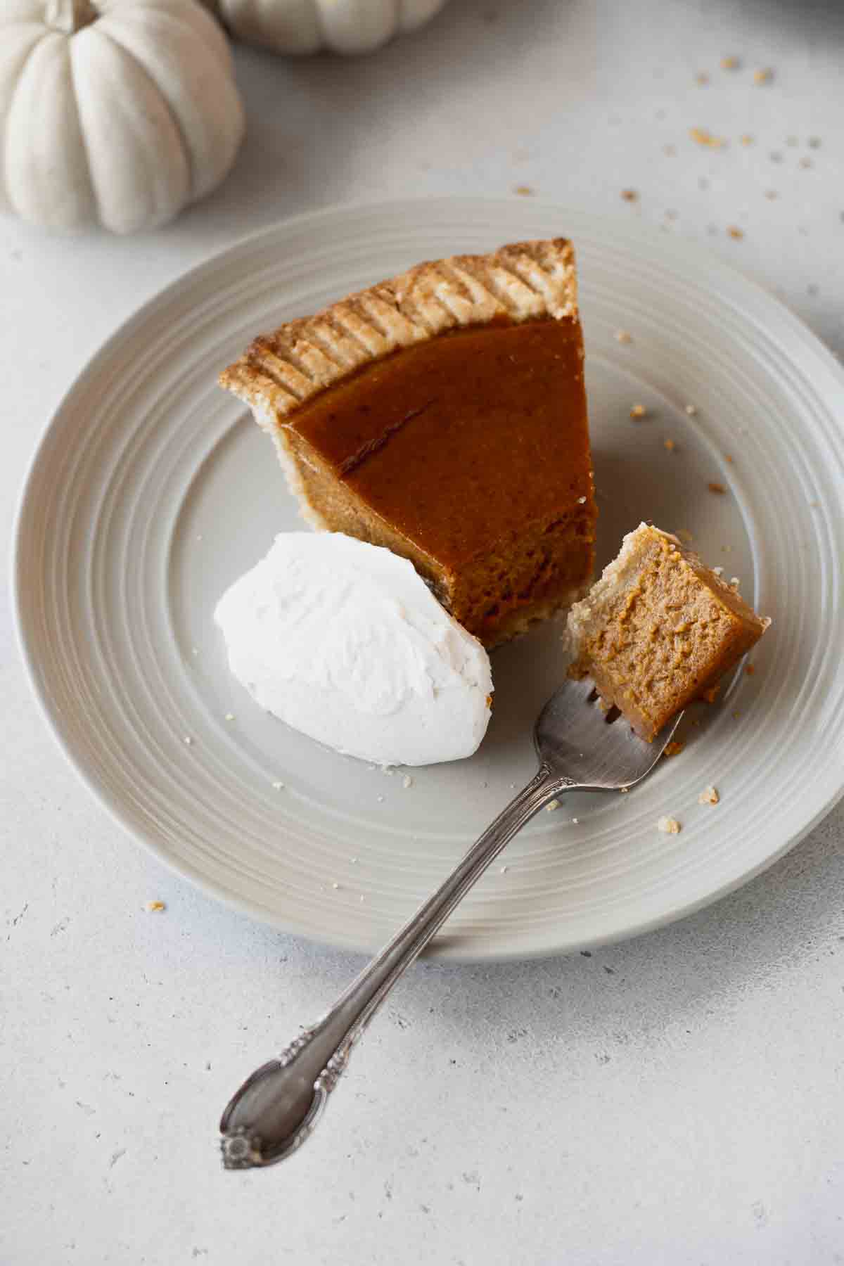 A slice of non-dairy pumpkin pie on a plate with a piece on a fork.