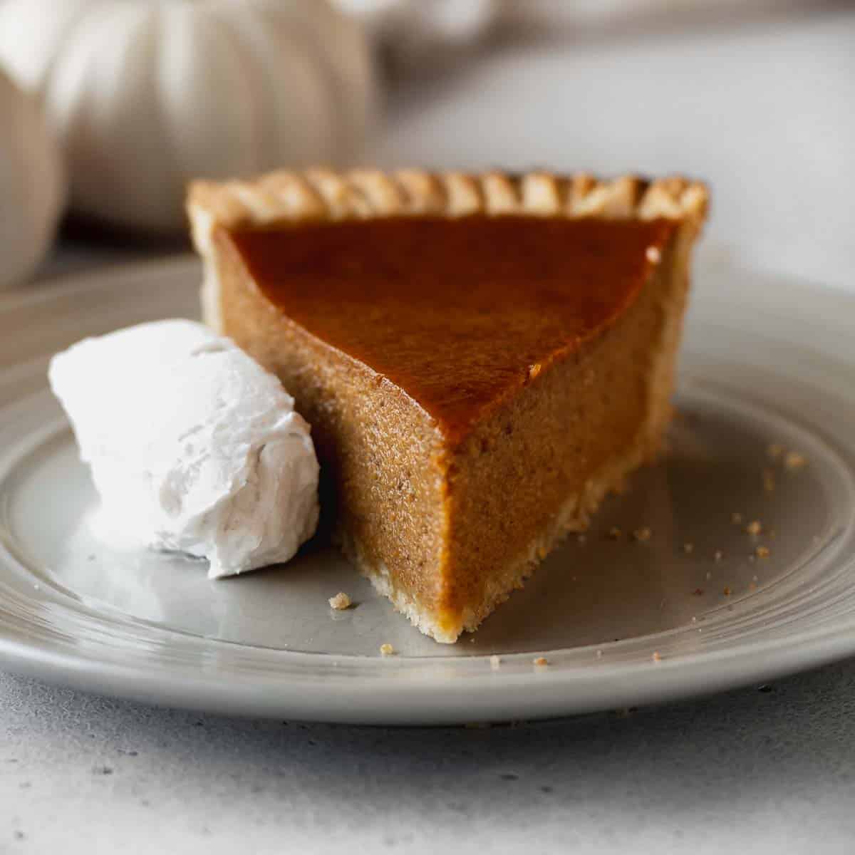 A slice of dairy-free pumpkin pie on a grey plate with a whipped coconut cream on the side.