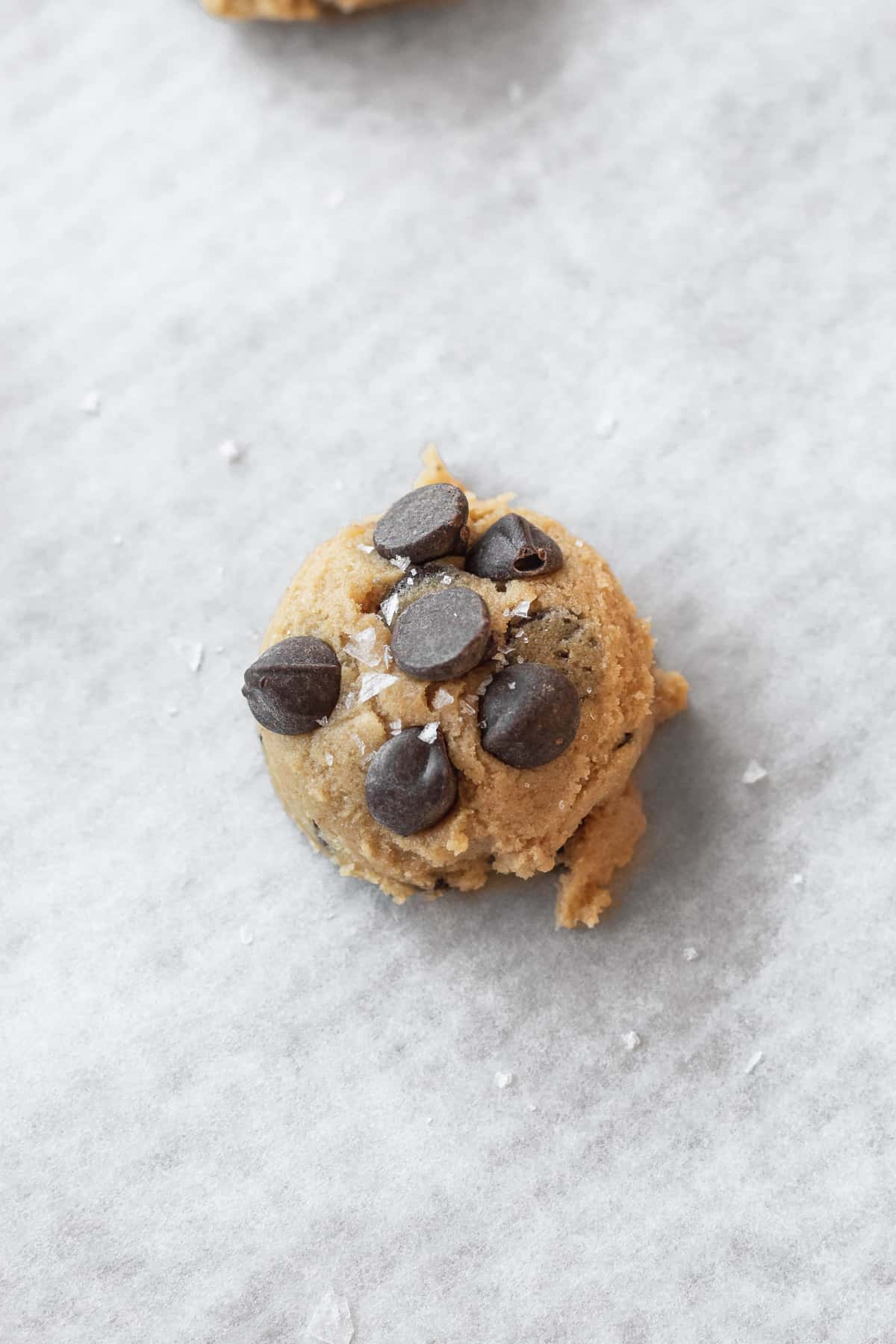 closeup of a ball of cookie dough that has been topped with extra chocolate chips and a sprinkle of coarse salt.