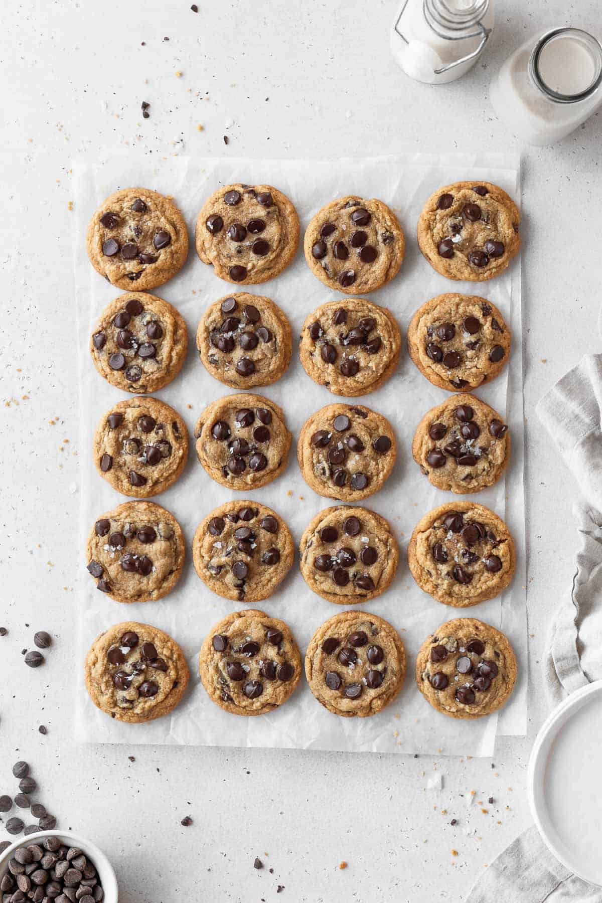 a parchment sheet topped with 20 freshly baked gf df chocolate chip cookies.