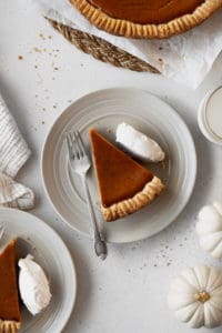 A slice of gluten free and dairy free pumpkin pie on a plate with whipped cream
