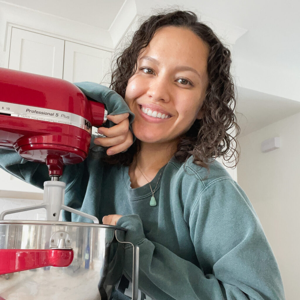 Ai Willis in a green sweatshirt smiling next to a red stand mixer.