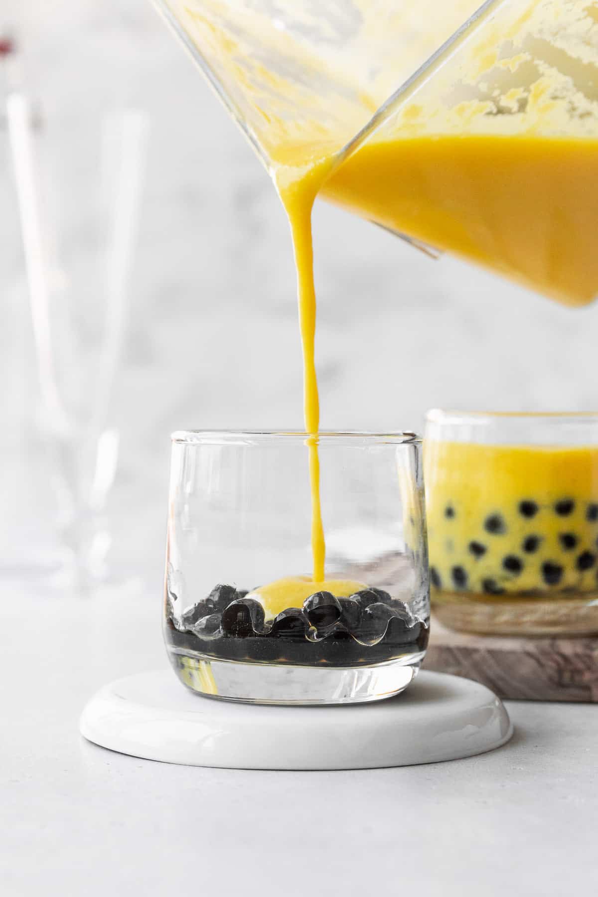 Pouring the mango puree into a small glass with the boba pearls.