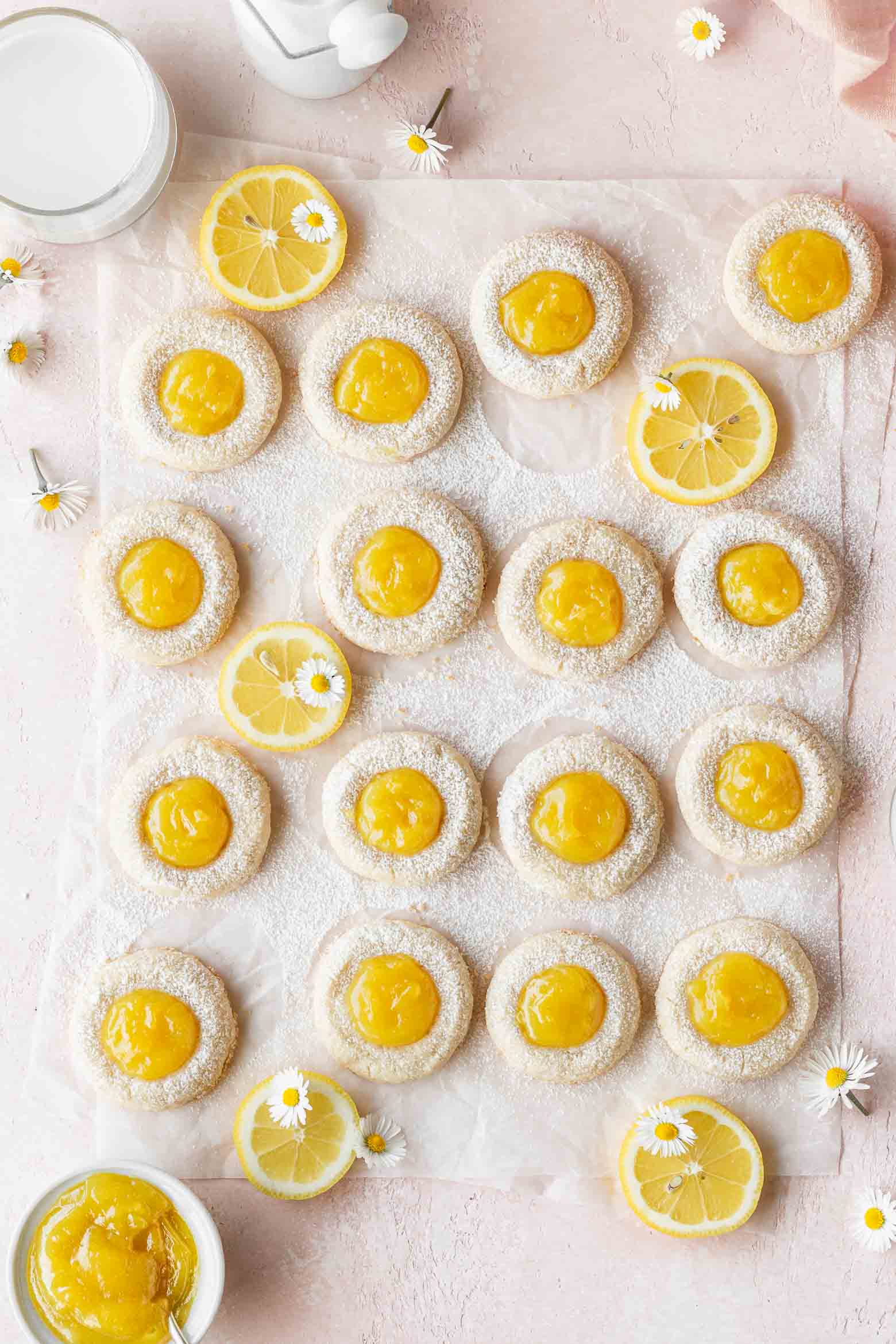 Overhead shot of vegan lemon cookies on parchment paper with slices of and small white flowers.