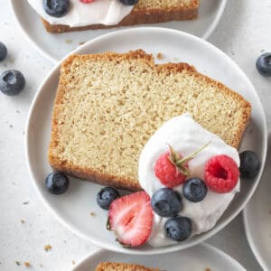A slice of gluten-free pound cake on a plate with whipped cream and berries.