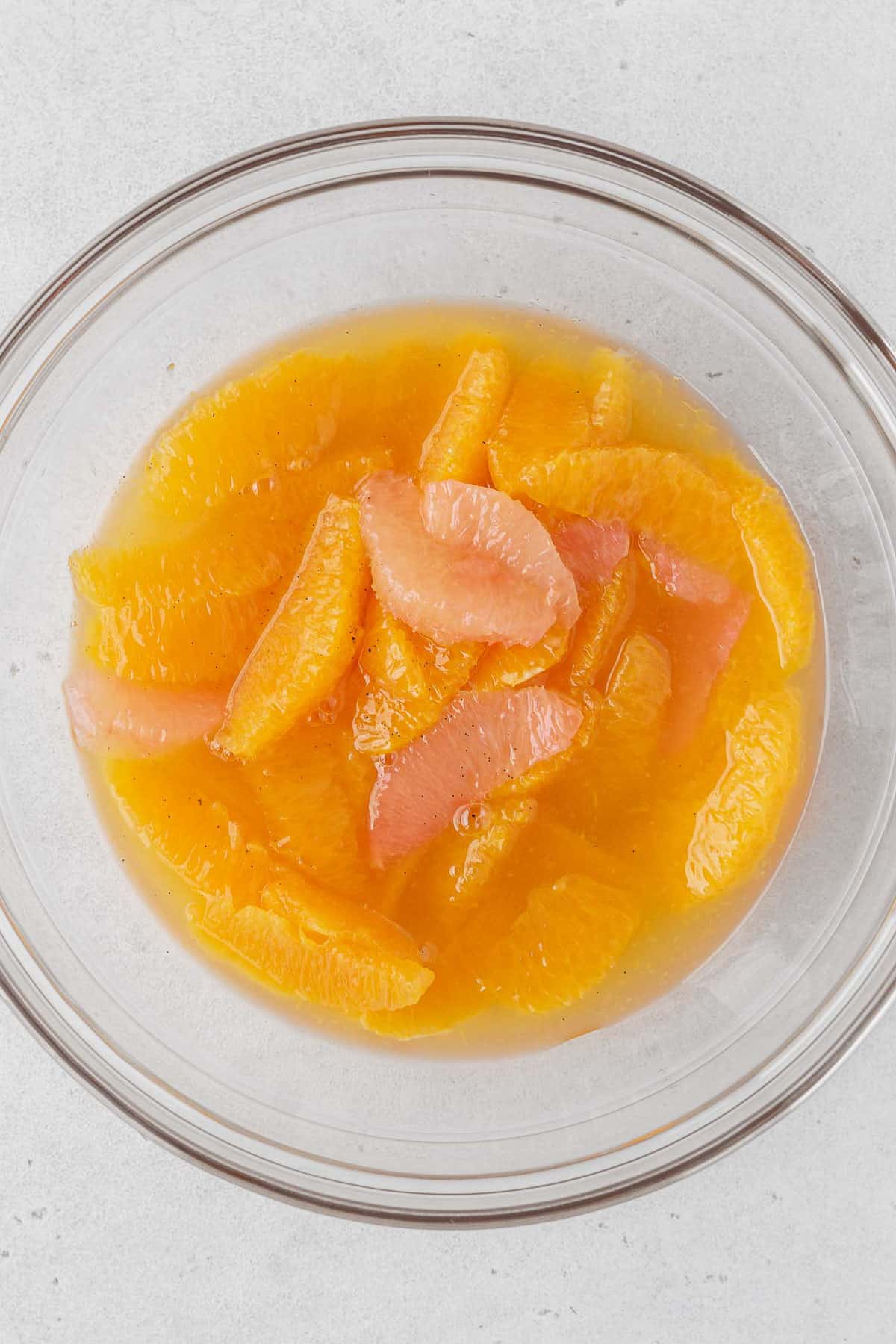 Orange and pink grapefruit segments in a glass bowl of syrup.