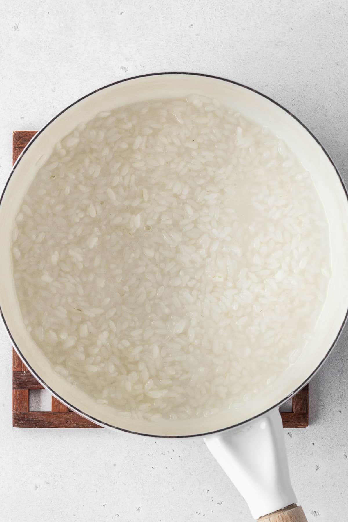 Rice cooking in a white saucepan of water.