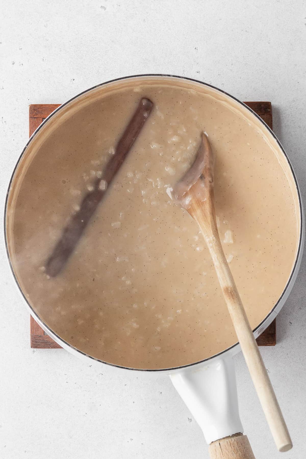 Cooked vegan rice pudding in a saucepan with a cinnamon stick and a wooden spoon.