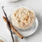 A bowl of vegan rice pudding with a cinnamon stick and vanilla bean