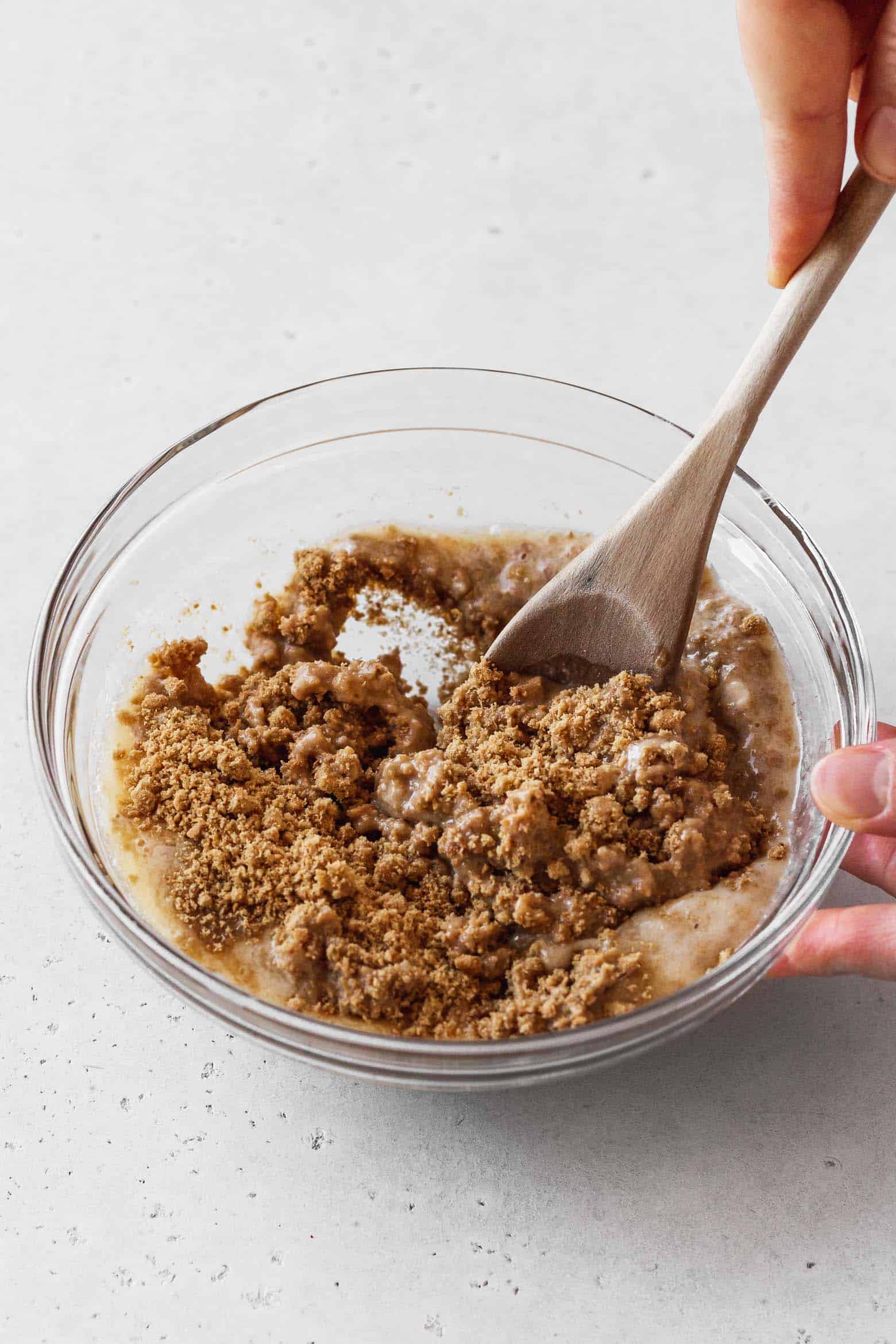 Mixing the graham cracker crumbs and butter with a wooden spoon.