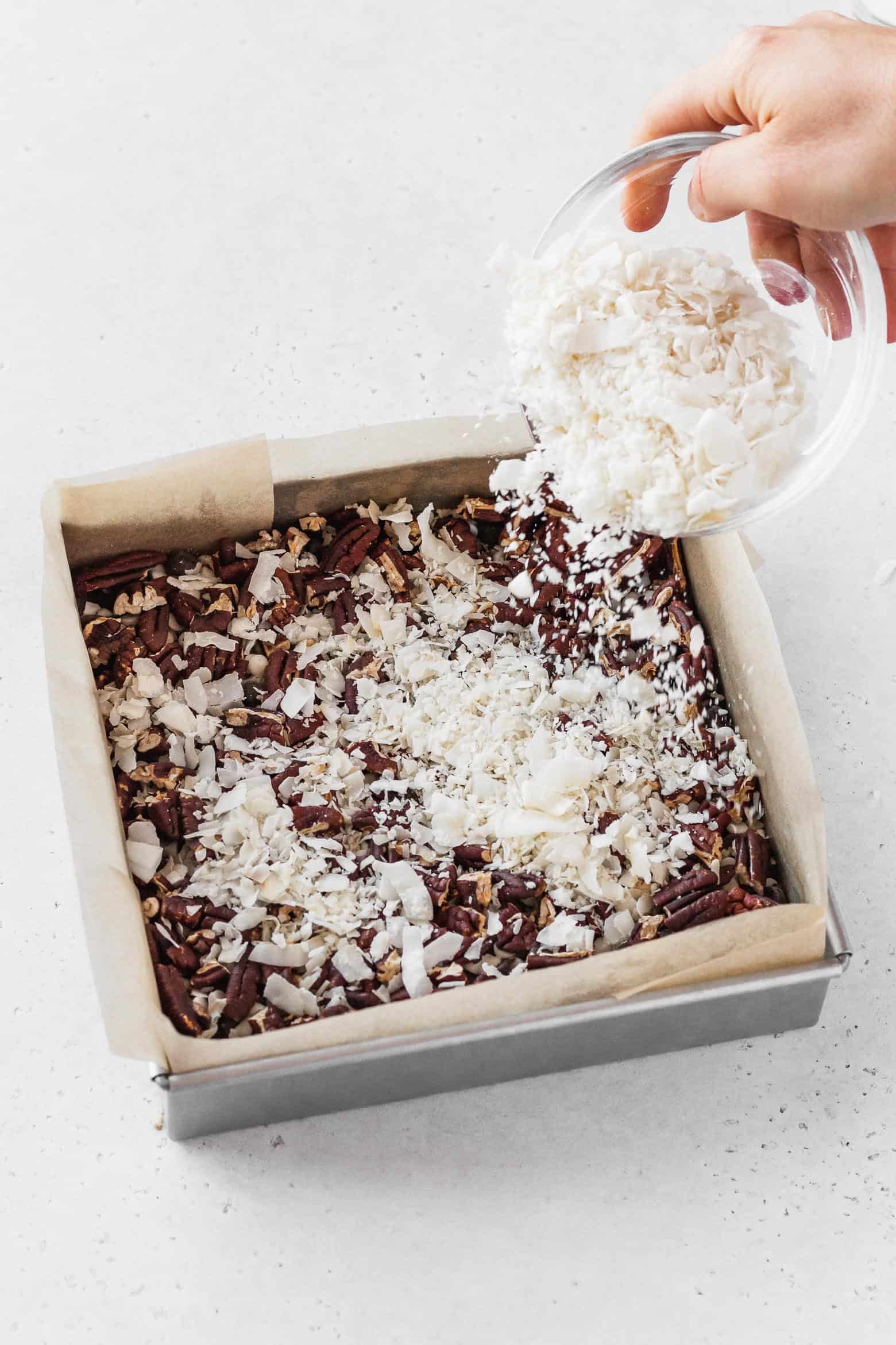 Sprinkling flaked coconut over the chopped pecans.