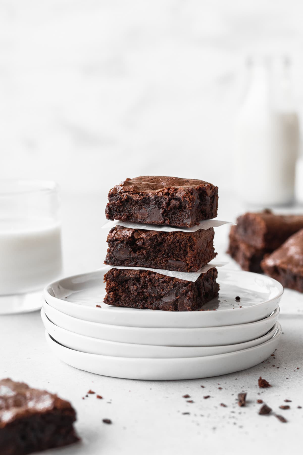 3 gluten-free chocolate brownies stacked on a stack of round white plates with more brownies and a jug of milk in the background.