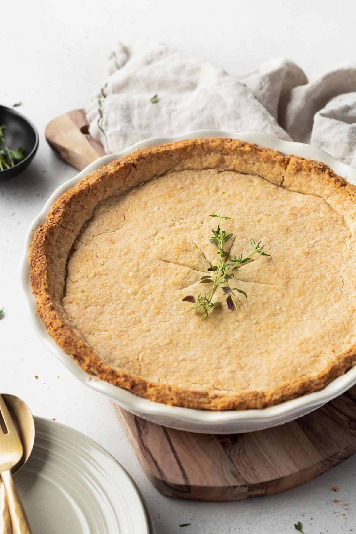 A whole vegan pot pie in a white ceramic pie dish with a few sprigs of thyme on top.