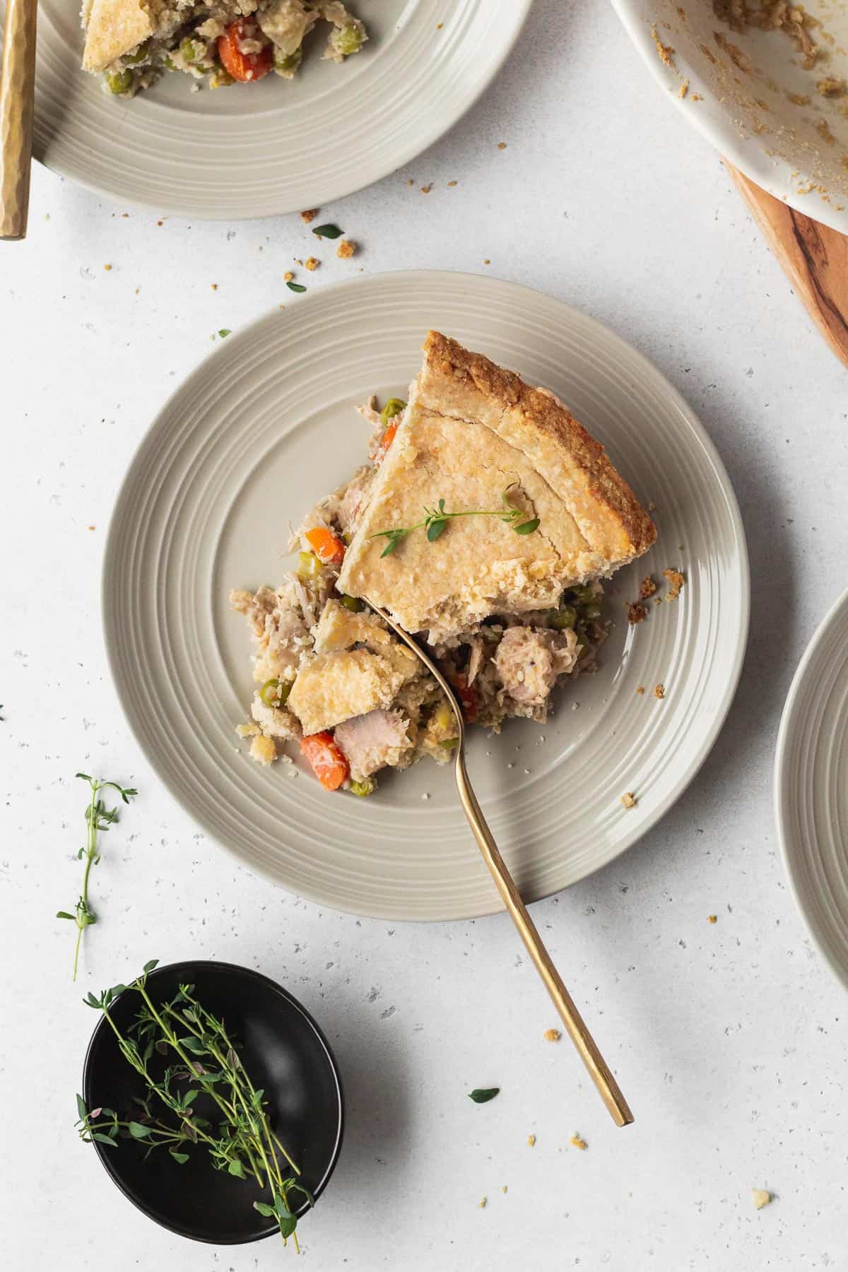 A slice of vegan chicken pot pie on a plate with a gold fork cutting through it.
