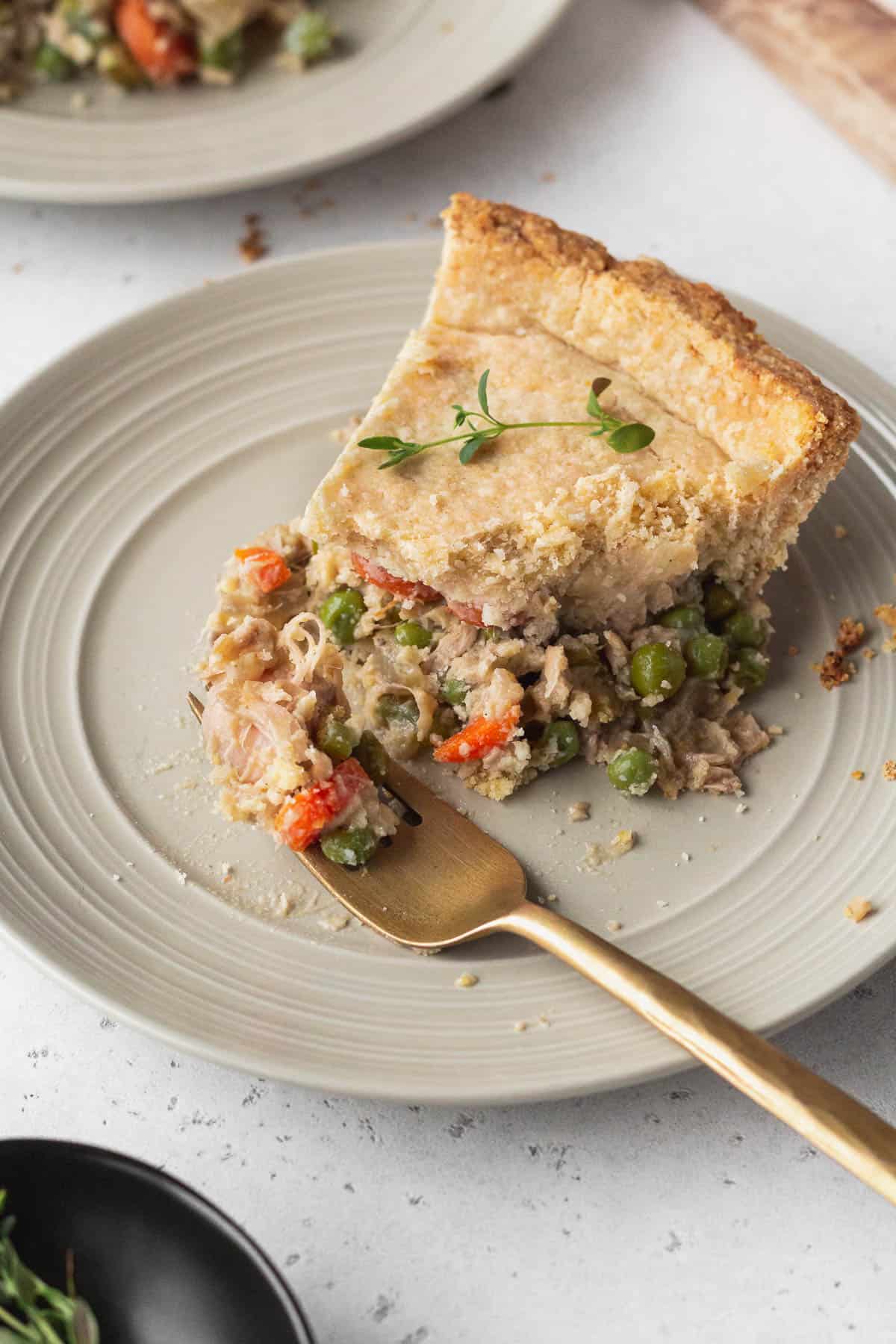 A slice of vegan chicken pot pie on a plate with a bite on a gold fork.
