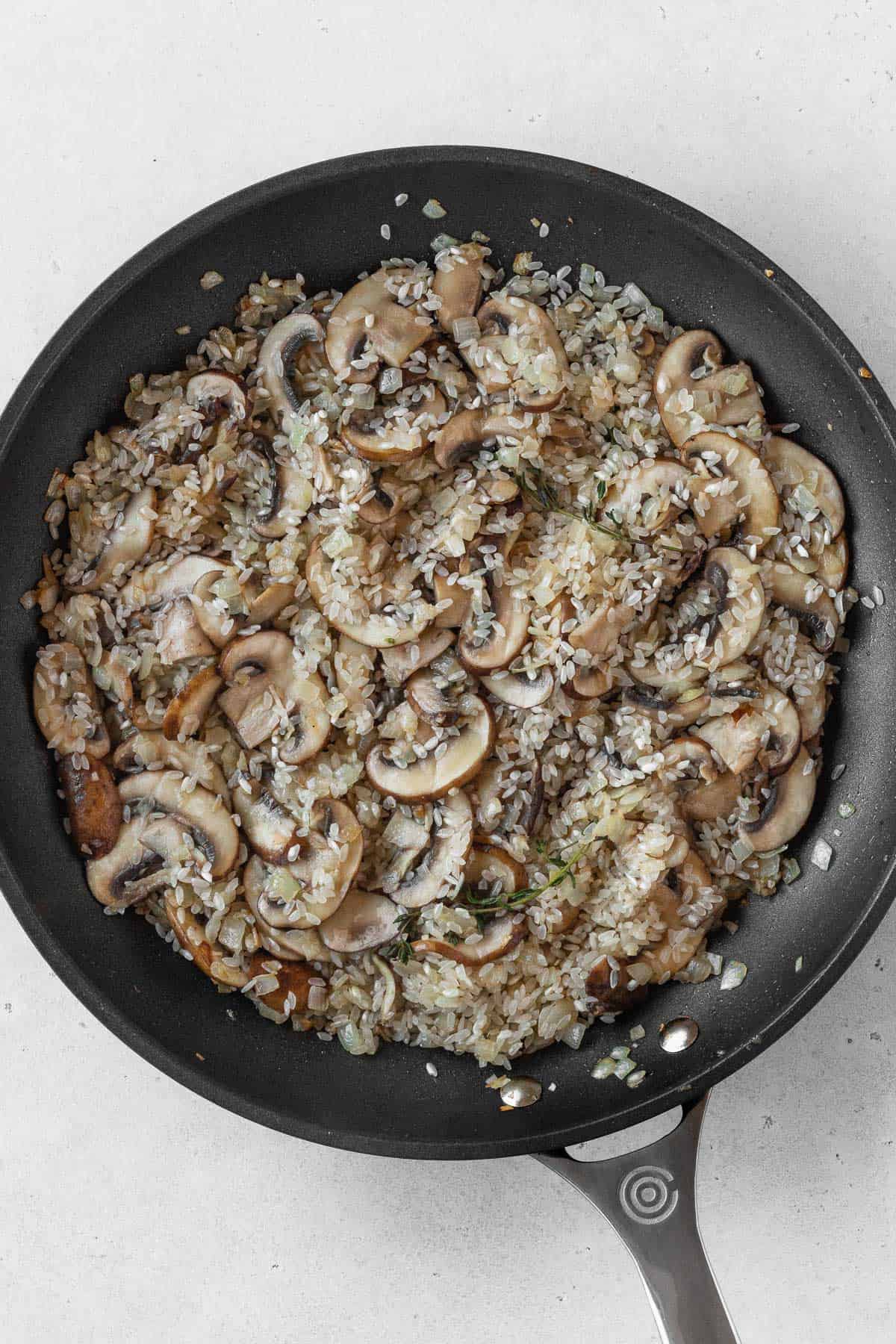 Onions, sliced mushrooms, and rice in a black pan.