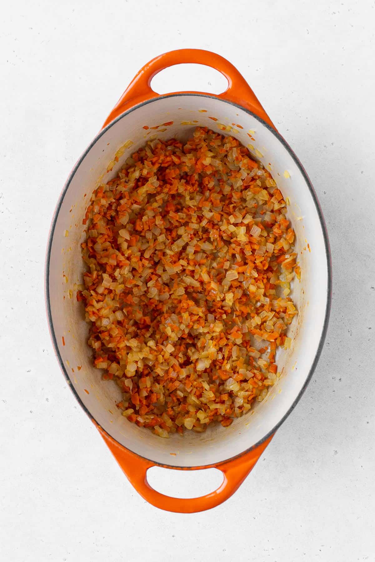 Minced onion and carrots cooking in an enameled pot.