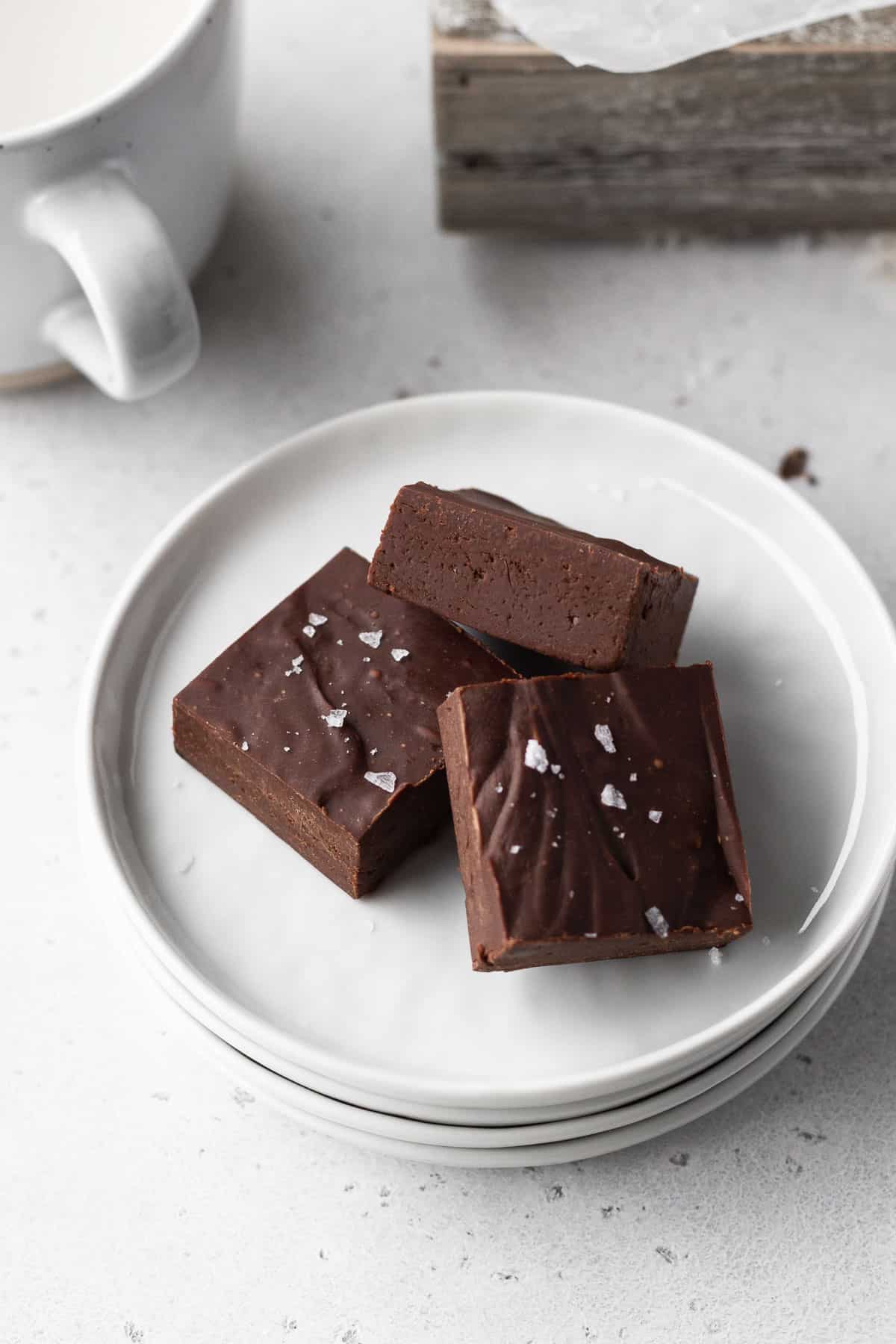3 squares of dairy free fudge on a white plate with a mug of plant-based milk to the side.