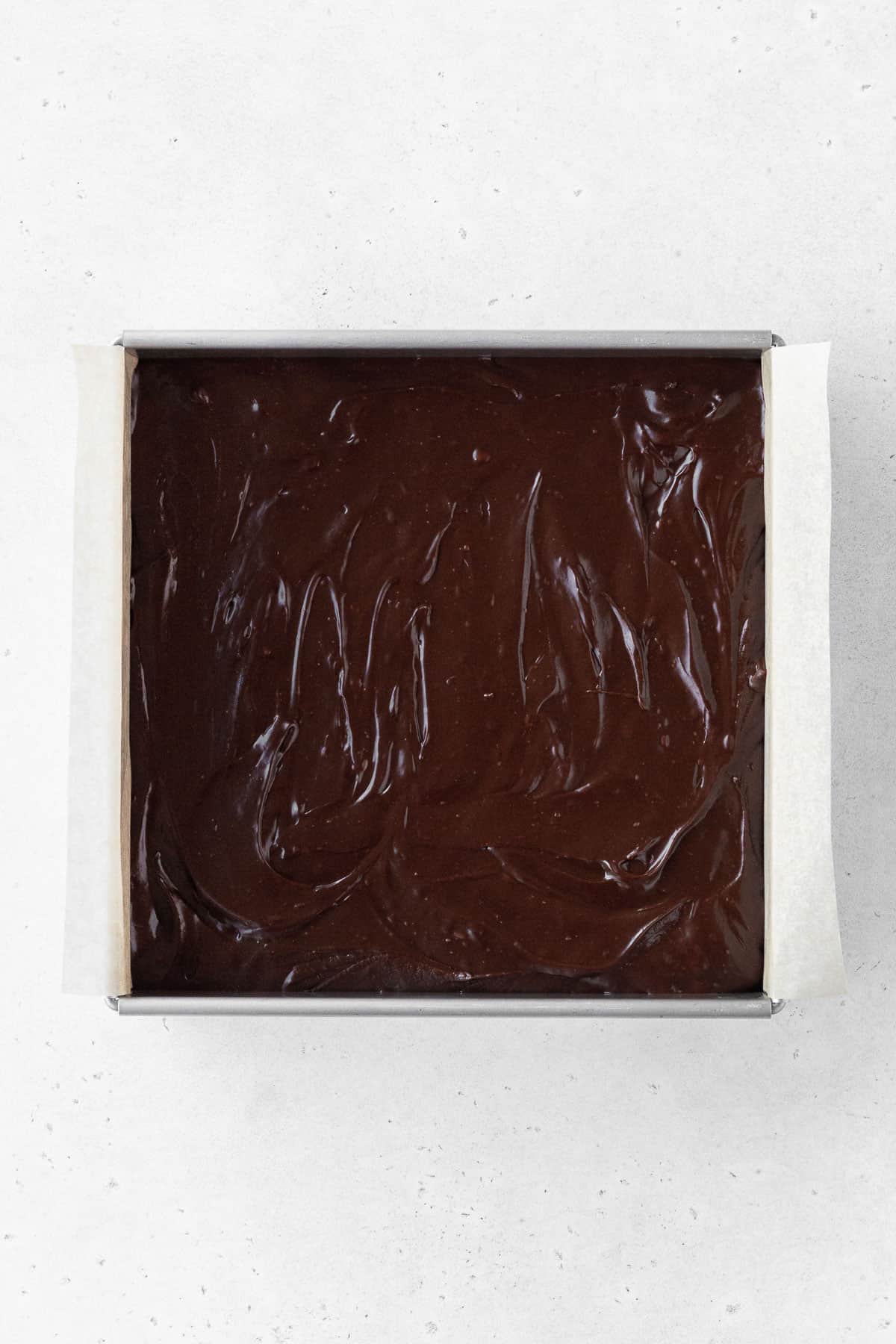 Dairy-free fudge batter poured into the parchment-lined baking tin and smoothed out with a spatula.