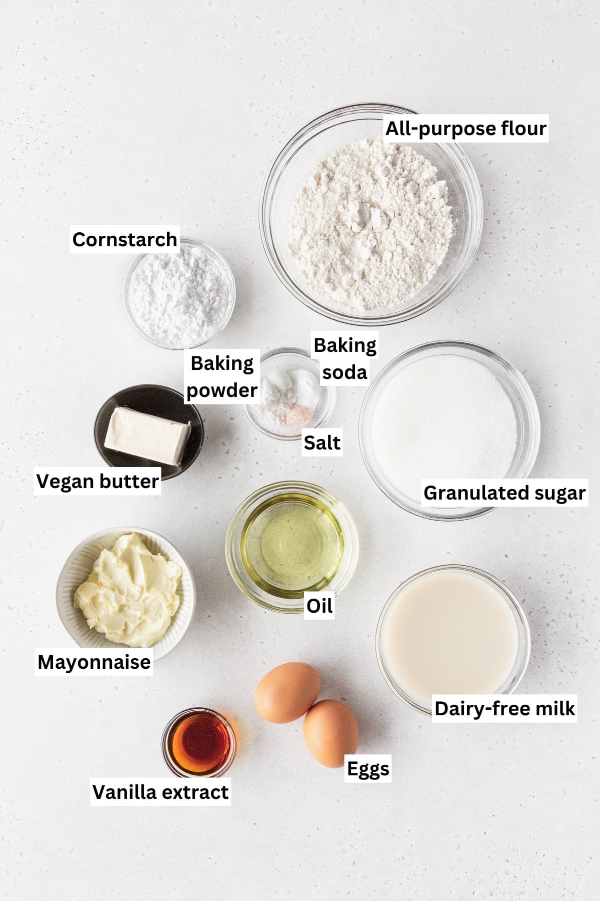 Ingredients for making dairy-free vanilla cupcakes laid out on a white table.