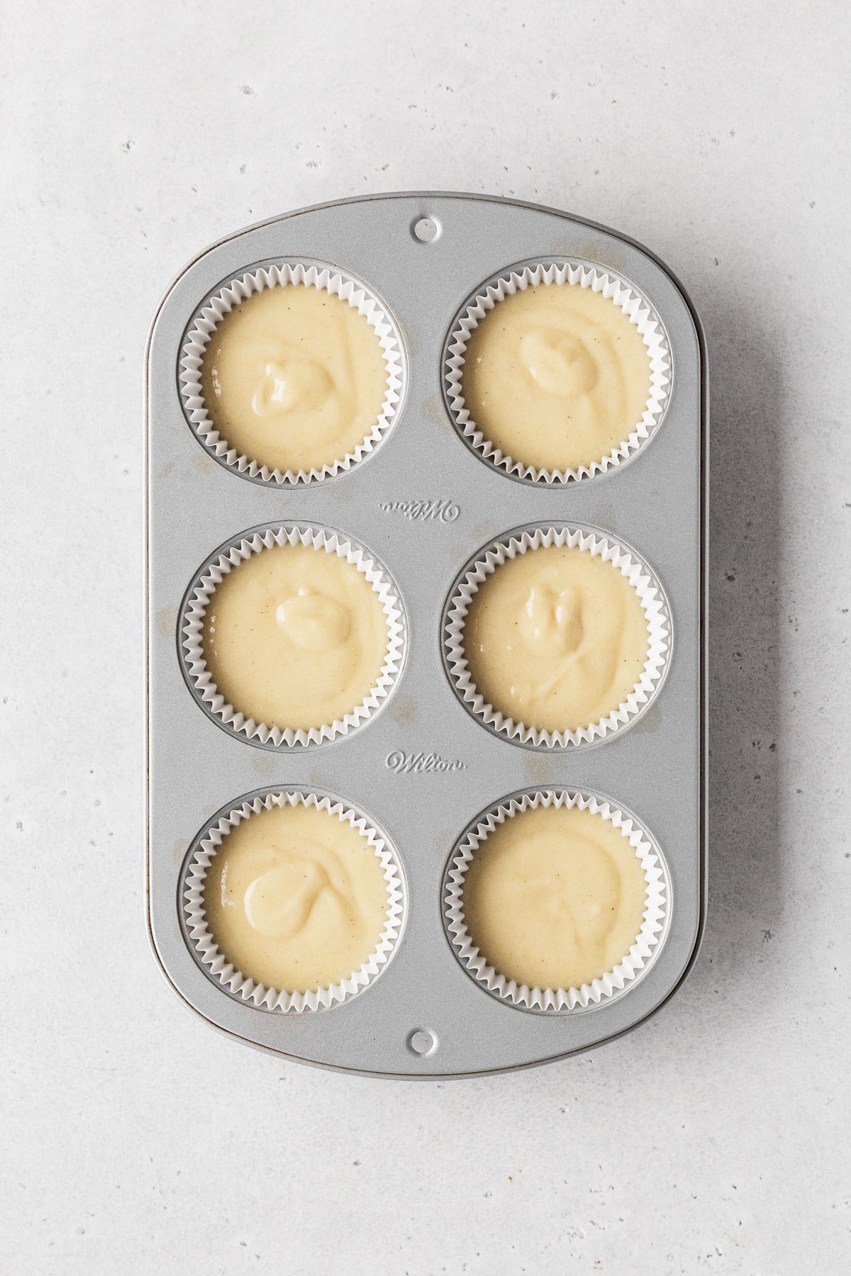 Muffin tin filled with white paper liners and dairy-free vanilla cupcake batter before baking.