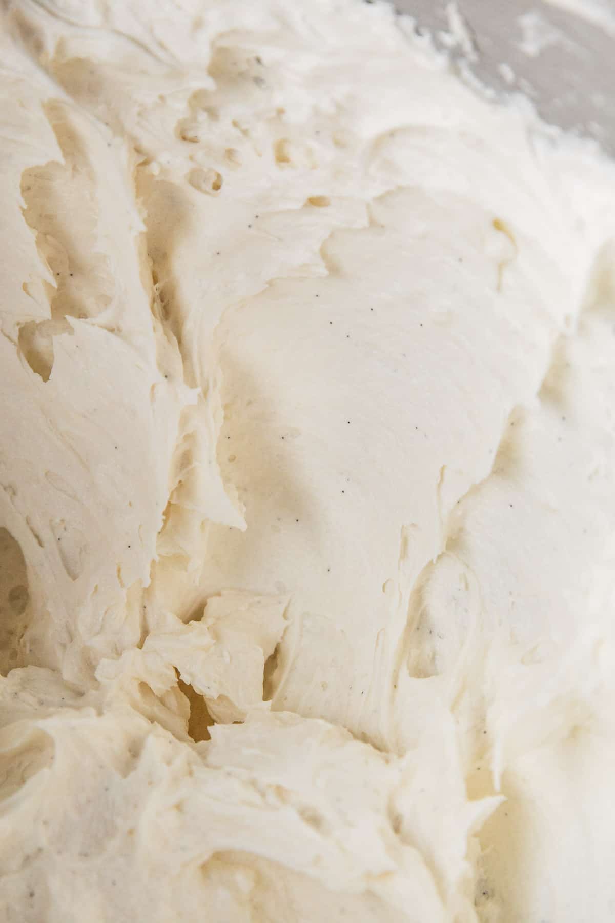 Closeup of the vegan vanilla buttercream frosting in the bowl, showing the delicate black flecks of vanilla bean throughout.