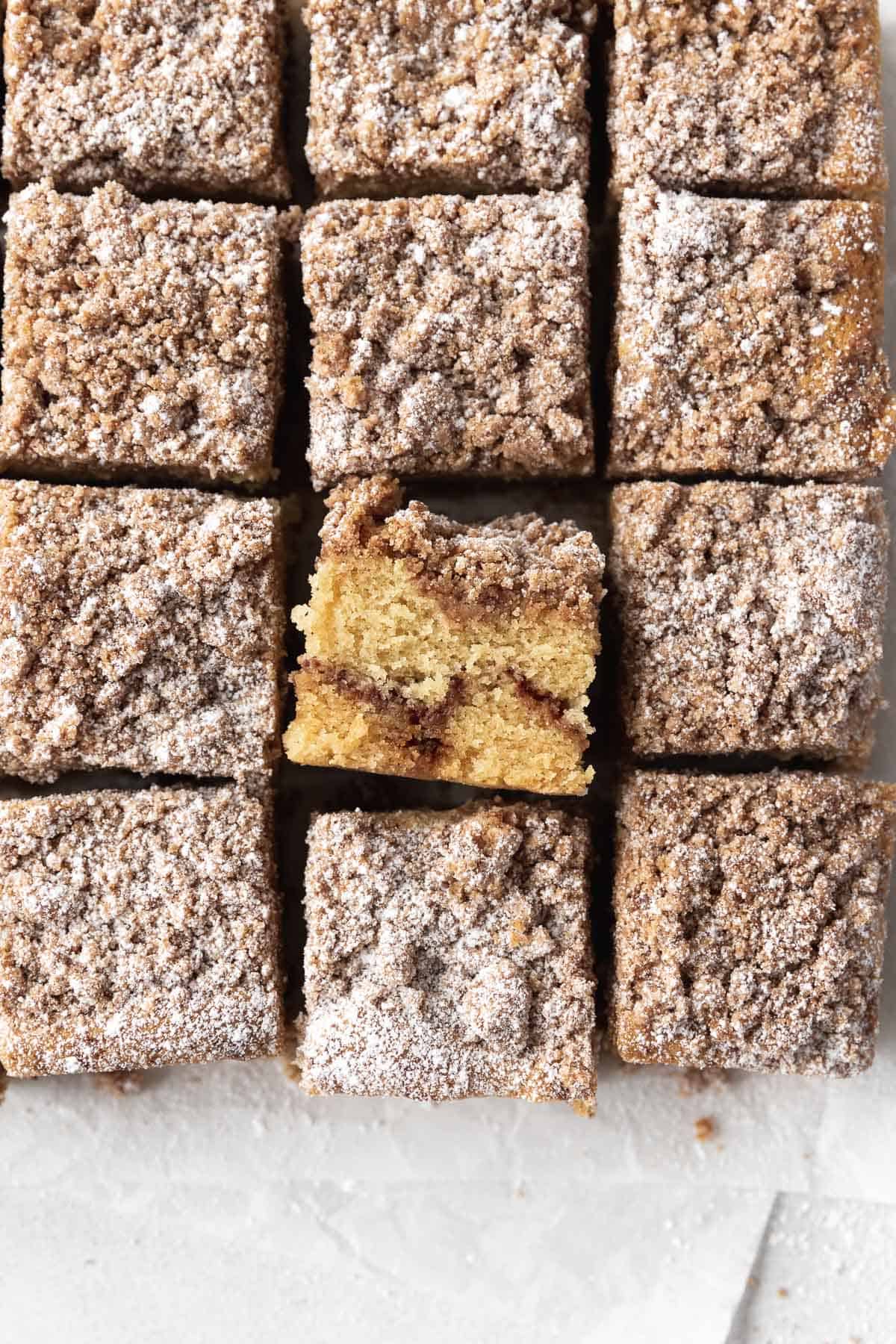 Overhead shot of gluten-free coffee cake cut into 12 squares with one flipped sideways to show the ribbon of cinnamon sugar filling running through it.