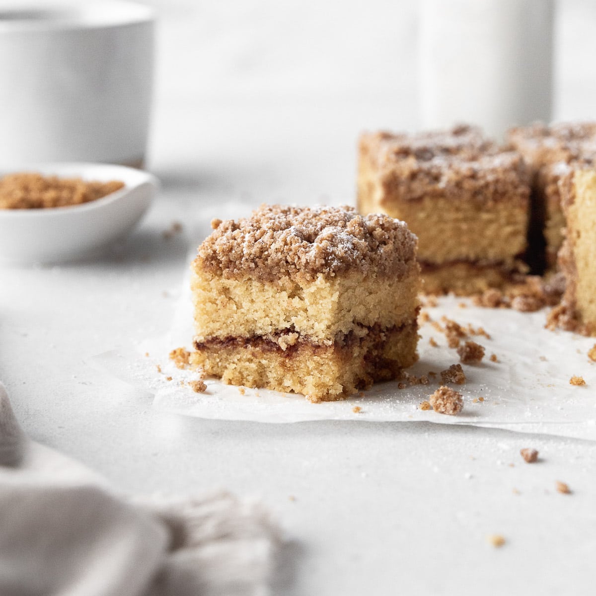 Square sideways hero shot of a square of fluffy, moist, gluten-free cinnamon coffee cake with a crumble topping.