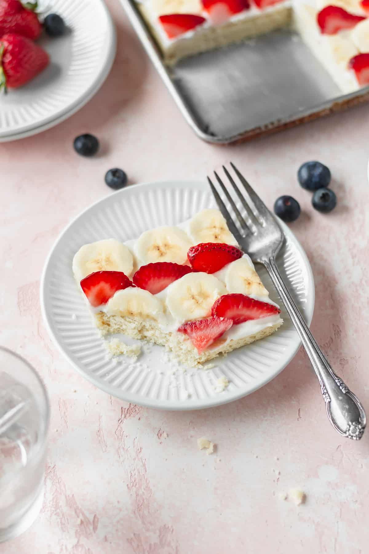 A slice of American flag fruit pizza on a dessert plate with a silver fork.