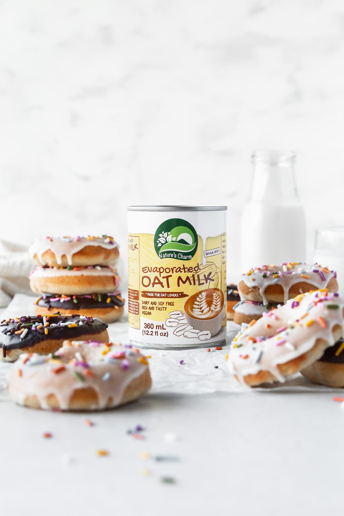 Can of Nature's Charm evaporated oat milk in the center of a table with vegan dairy-free donuts all around.