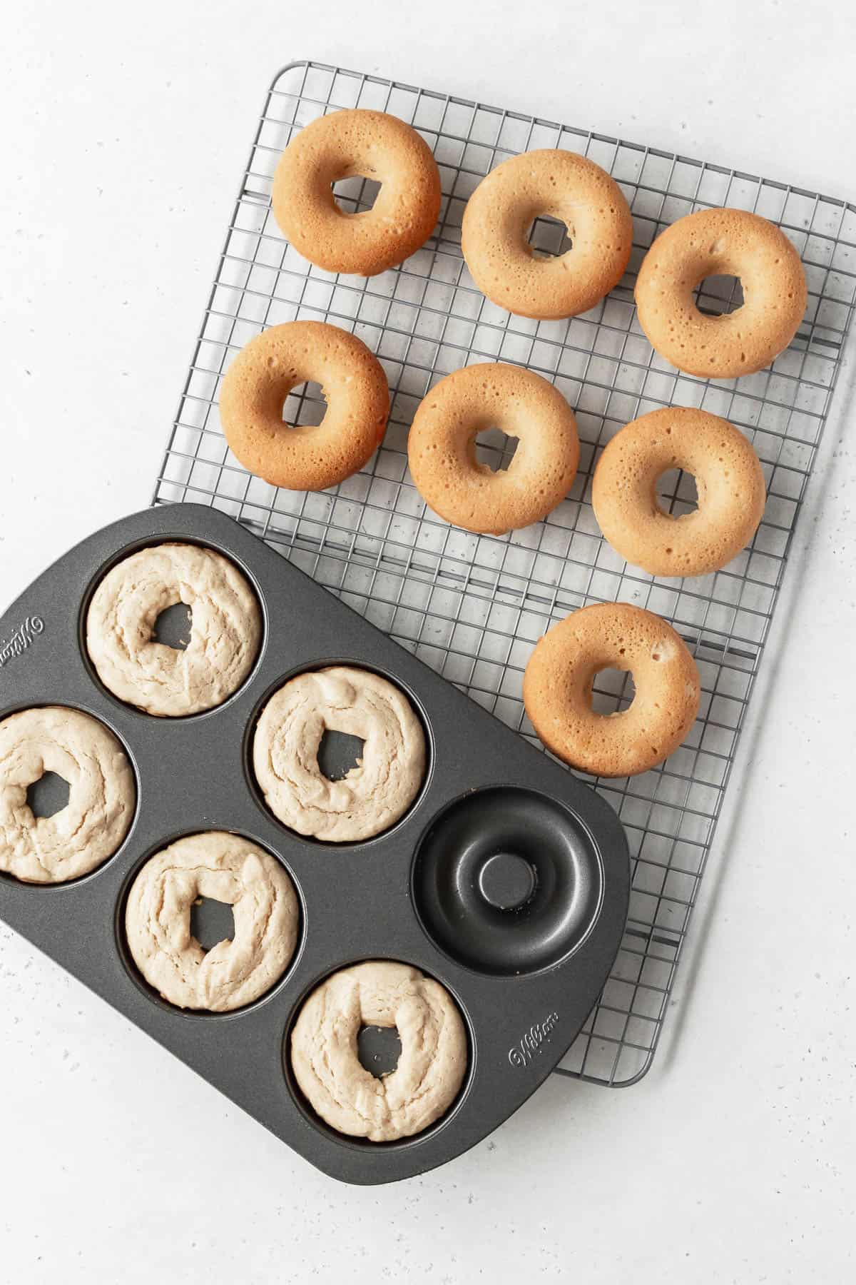 Overhead shot of a pan of gluten free dairy free doughnuts on a wire rack with more donuts that have been removed the pan are cooling.
